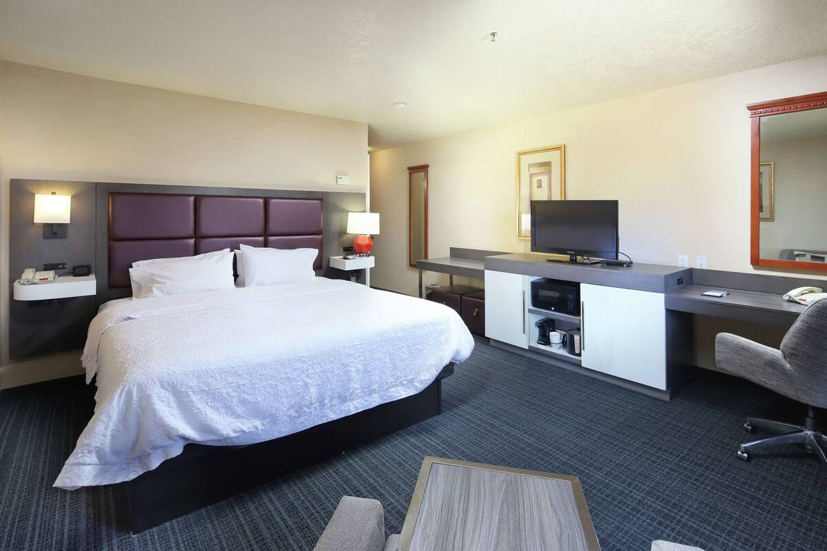 A hotel room with a large bed, a desk with a computer, a TV, and a mirror.
