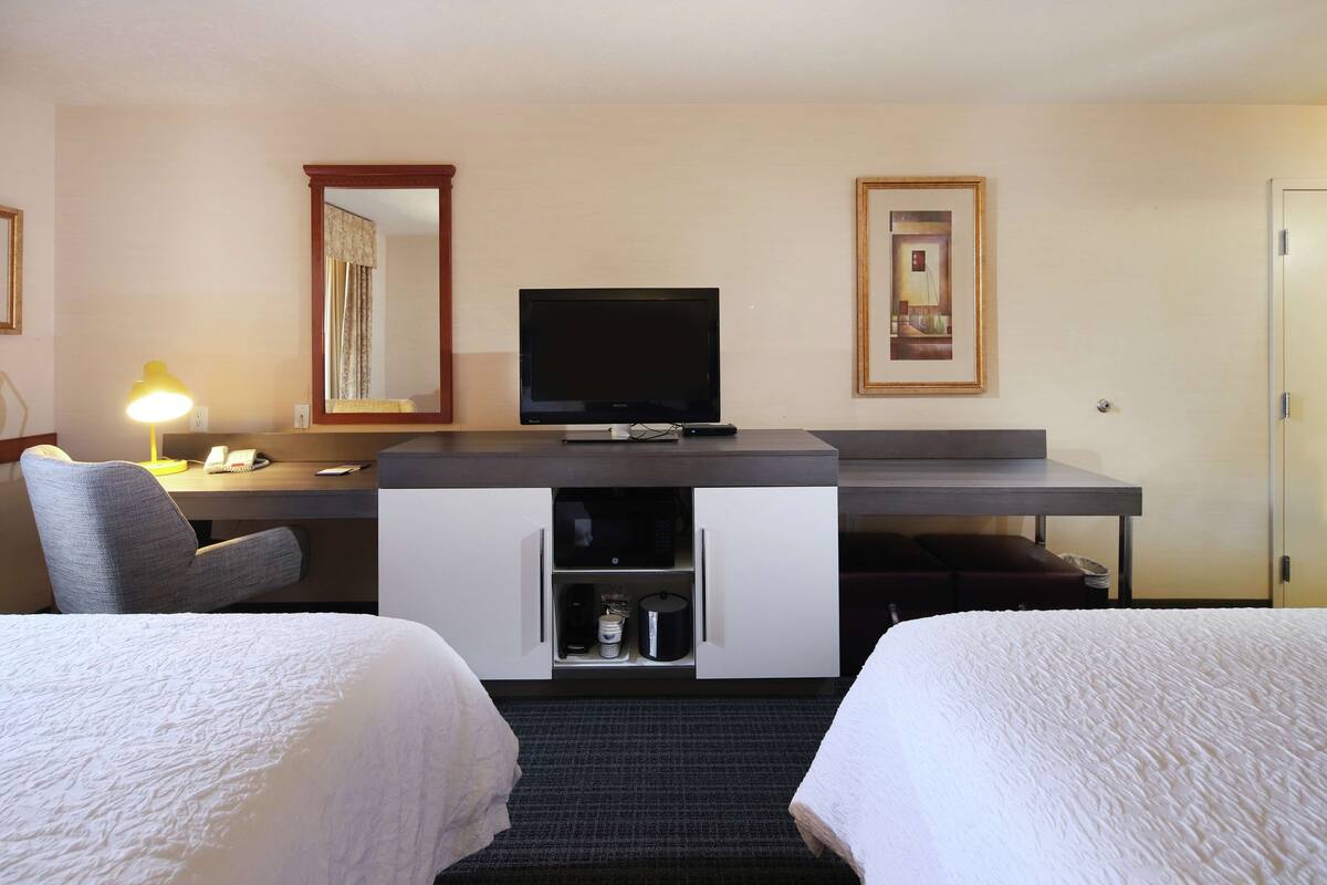 A hotel room with a bed, a desk with a computer, a TV, and a lamp.