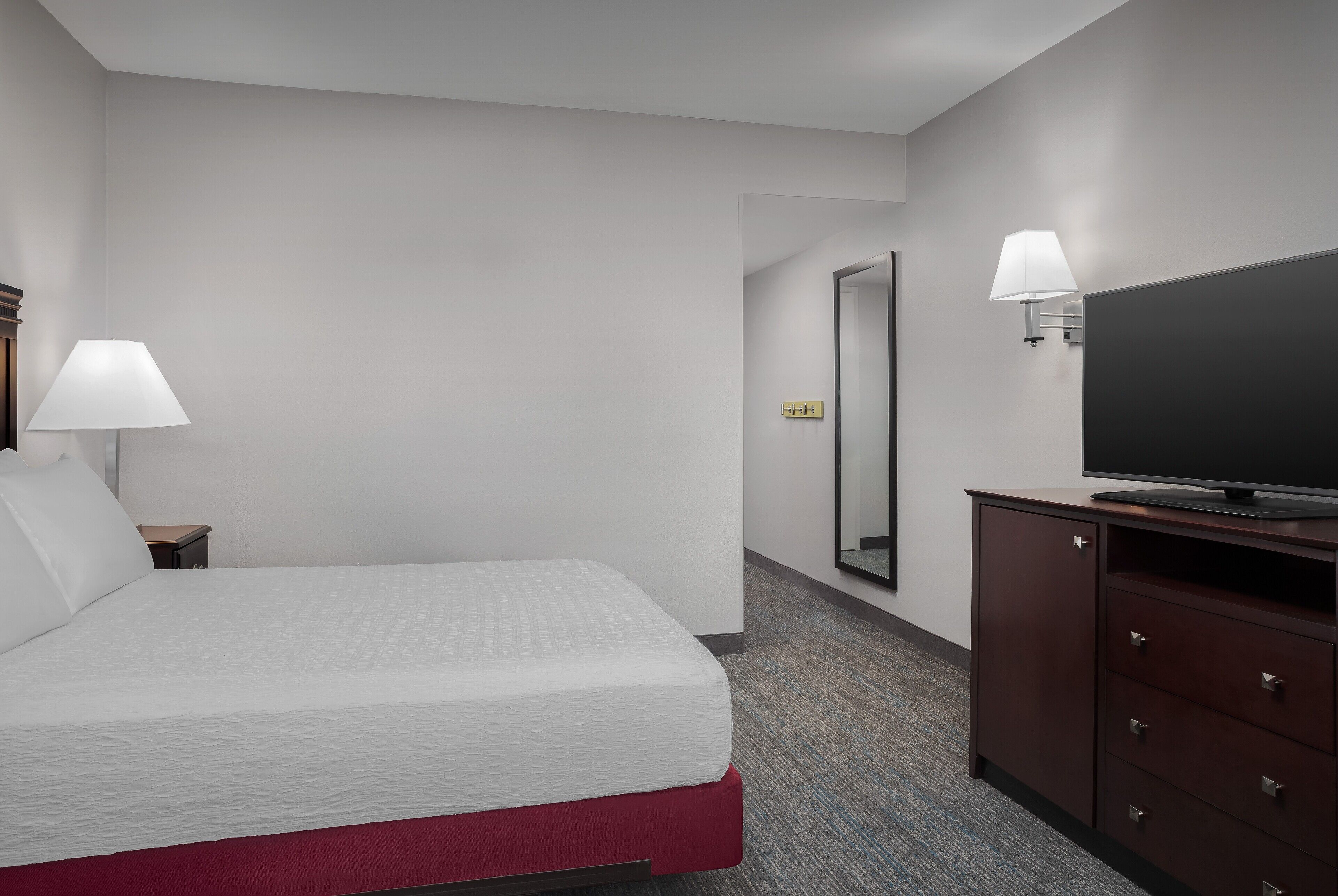 Een hotelkamer met een bed, een televisie op een kast en een lampje op het nachtkastje.