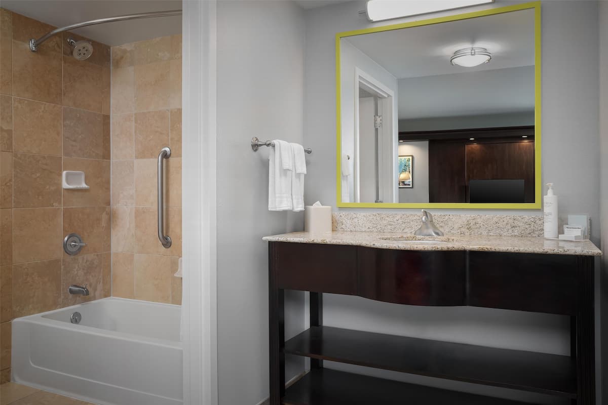 A bathroom with a bathtub, a shower, a vanity with a mirror, and a towel rack.