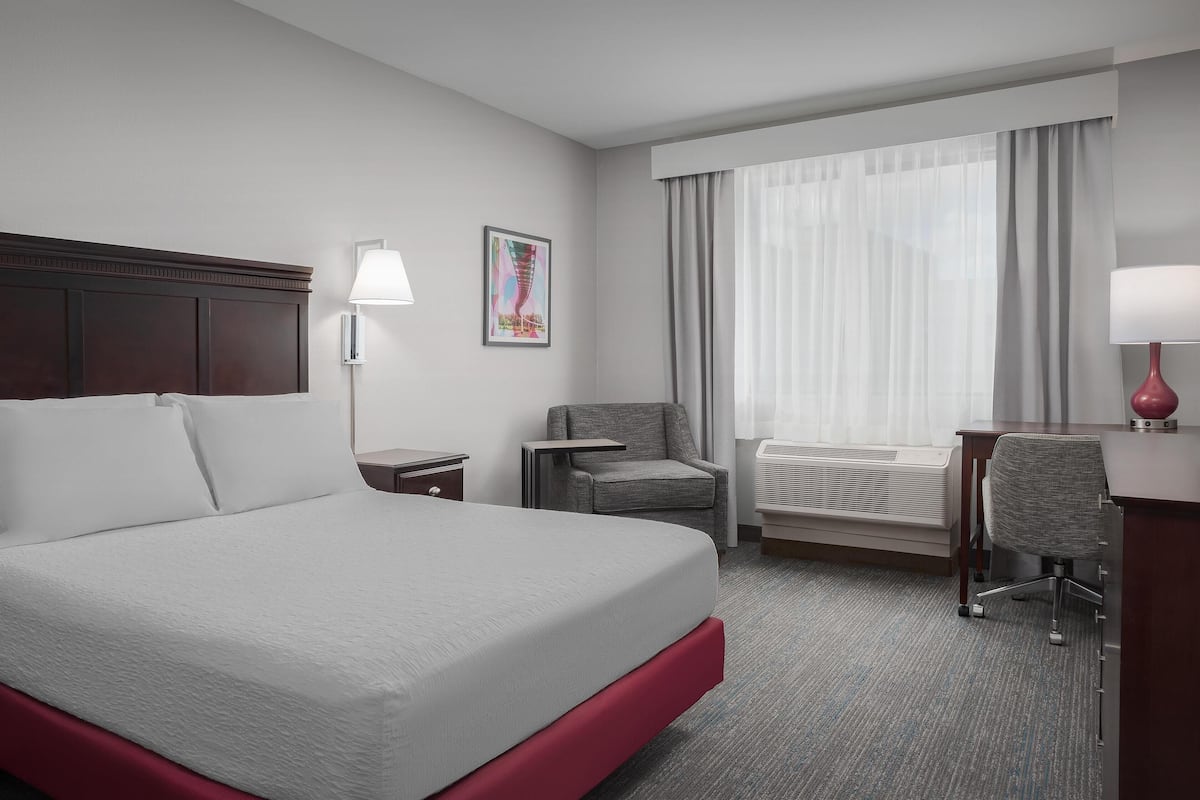 A hotel room with a large bed, a desk, a chair, a lamp, and a window with curtains.