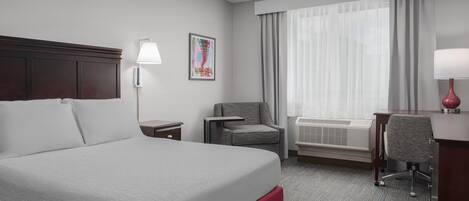 A hotel room with a large bed, a desk, a chair, a lamp, and a window with curtains.