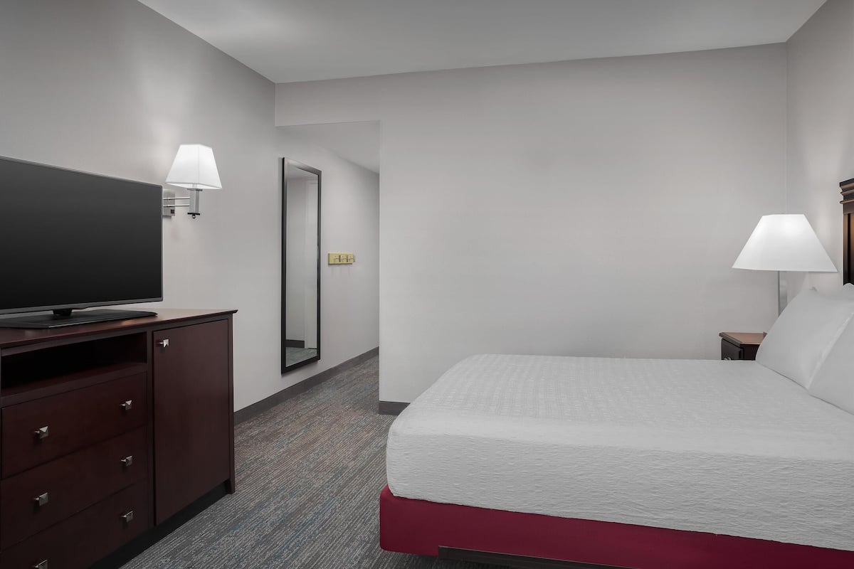 A hotel room with a bed, a TV on a wooden cabinet, a mirror, and two wall-mounted lamps.