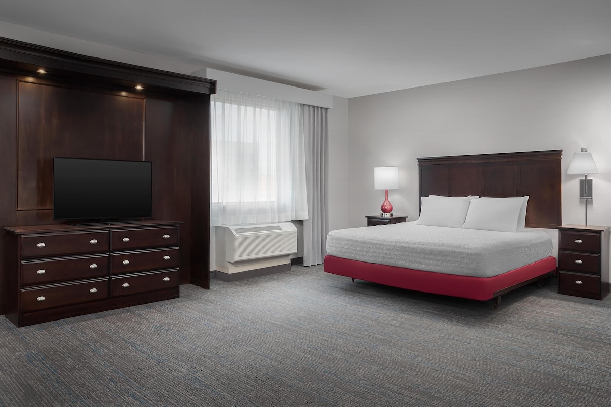 A hotel room with a large bed, a TV, a dresser, and a window with curtains.