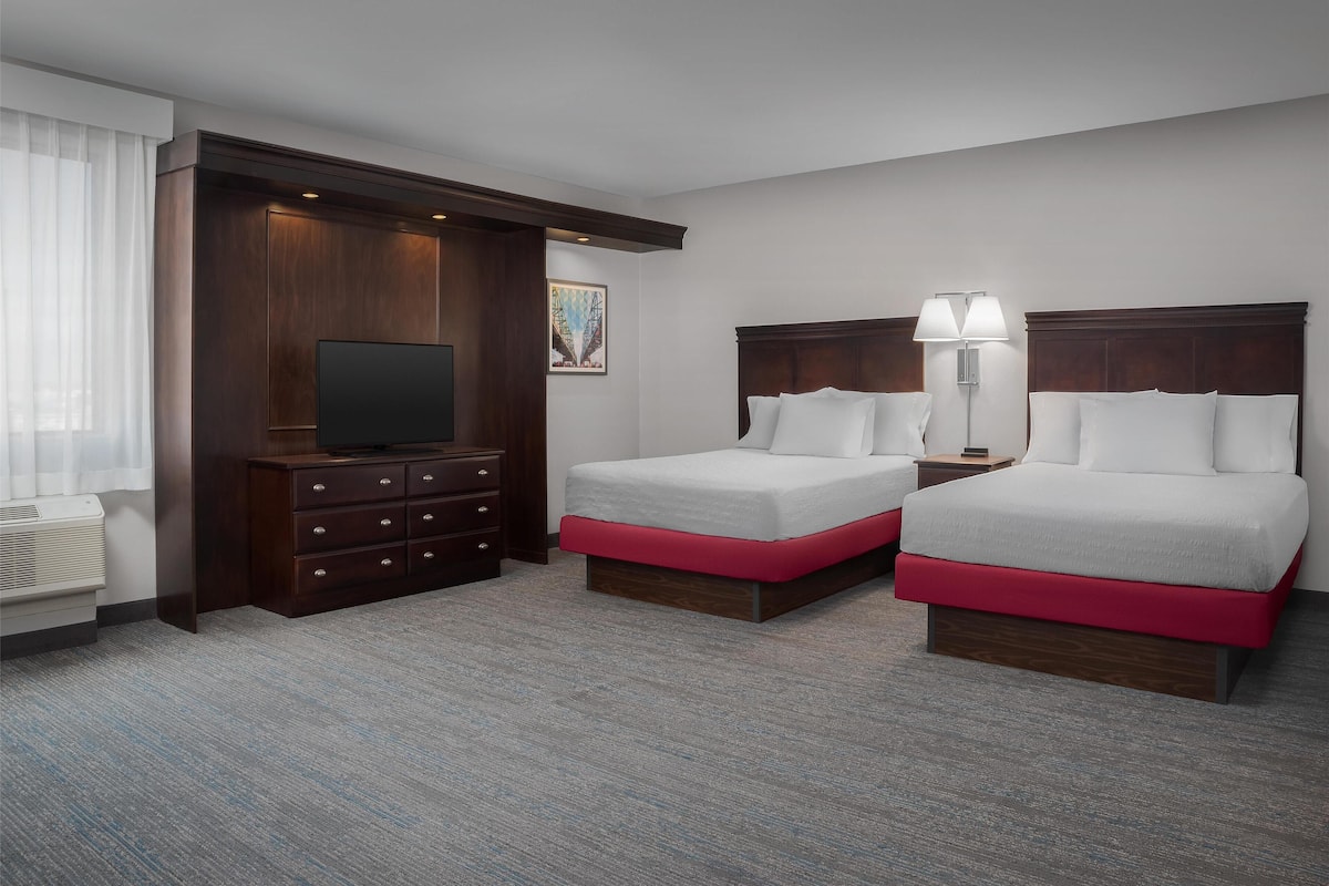 A hotel room with two beds, a TV, a dresser, and a lamp.