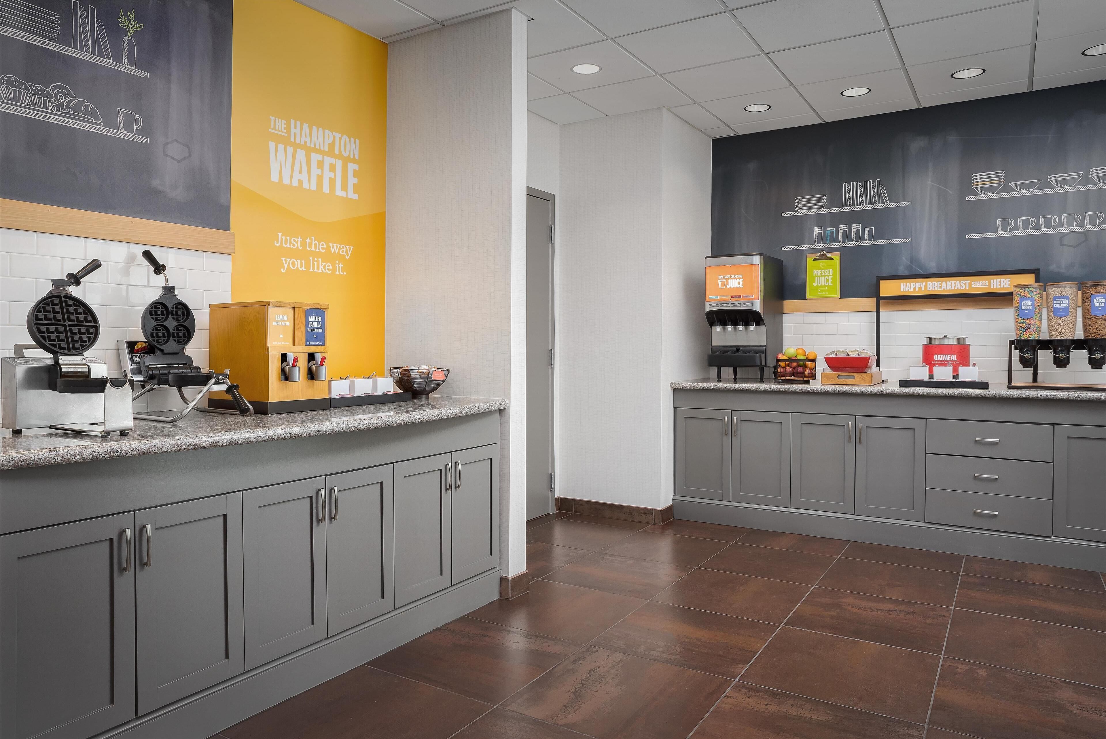 A modern kitchen area with waffle makers, a juice dispenser, and a breakfast bar.