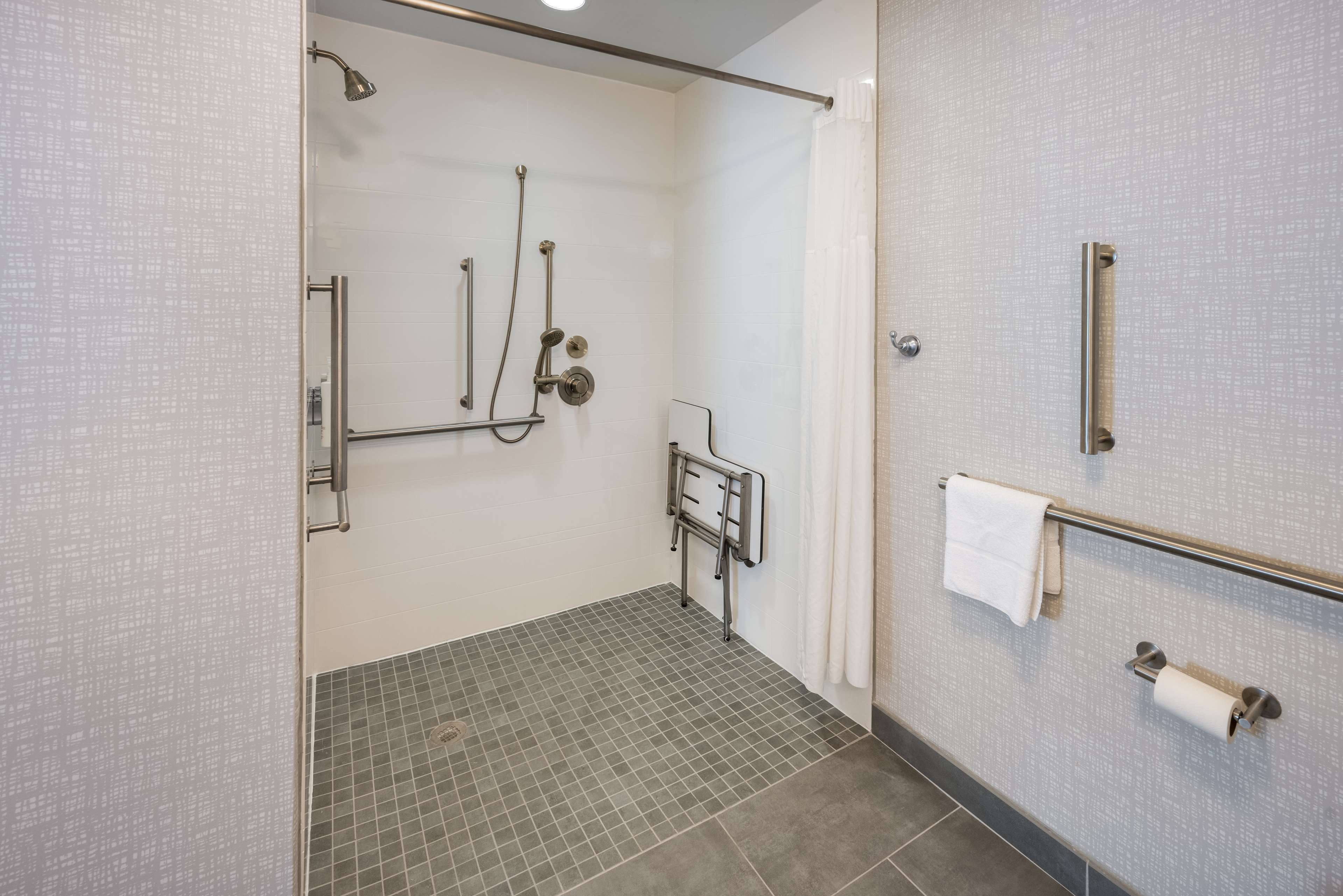 Un espace douche doté d’une porte en verre, d’une barre d’appui, d’un porte-serviettes et d’un support à papier toilette.