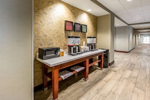 Un hall de hotel con una estación de café, microondas y obras de arte enmarcadas en la pared.
