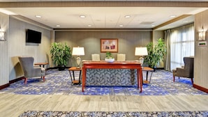 A conference room with a wooden table, two chairs, a potted plant, a wall-mounted TV, and a patterned carpet.