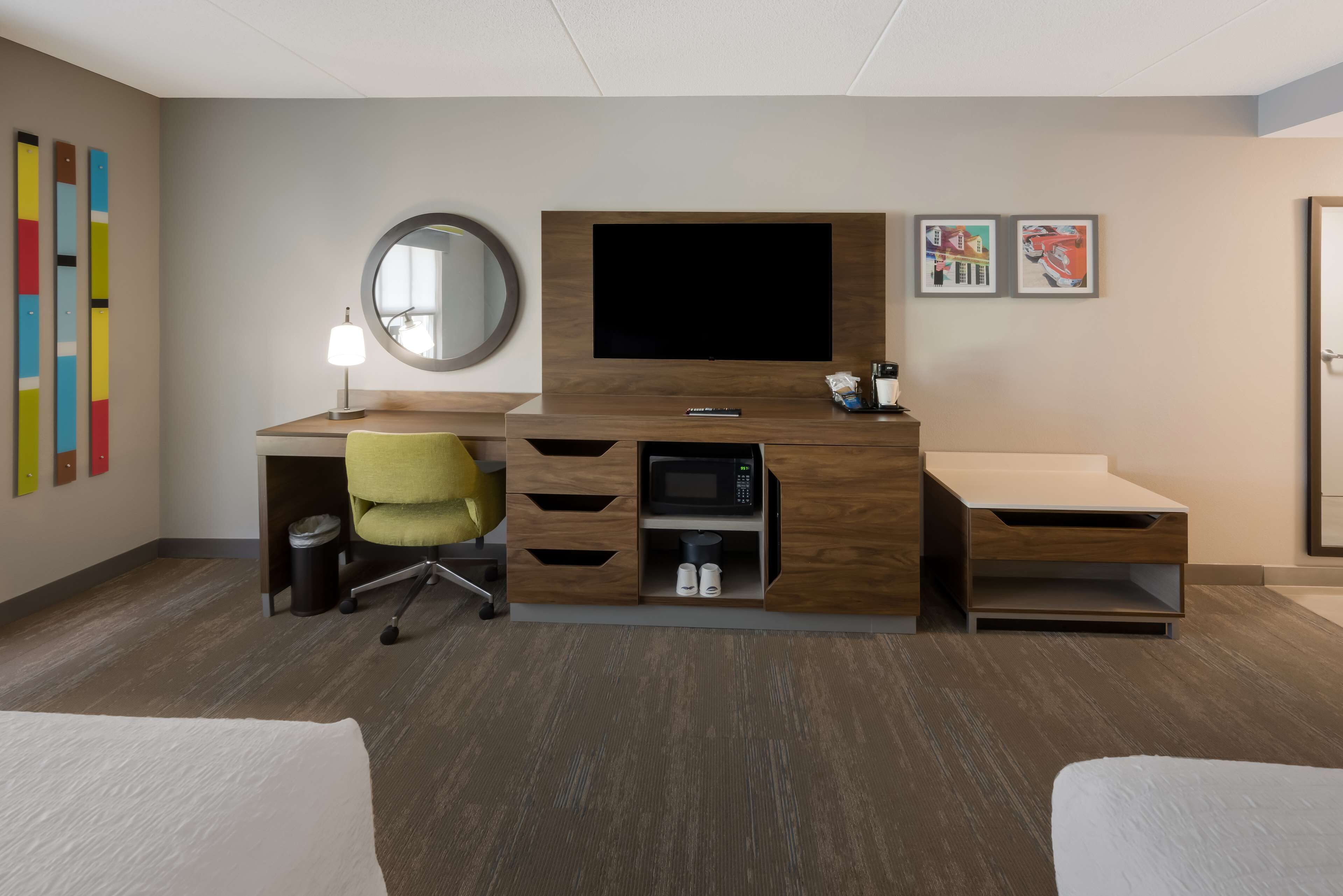 Ein modernes Hotelzimmer mit einem Holztisch, einem Flachbildfernseher, einer Mikrowelle und einer kleinen Sitzecke.