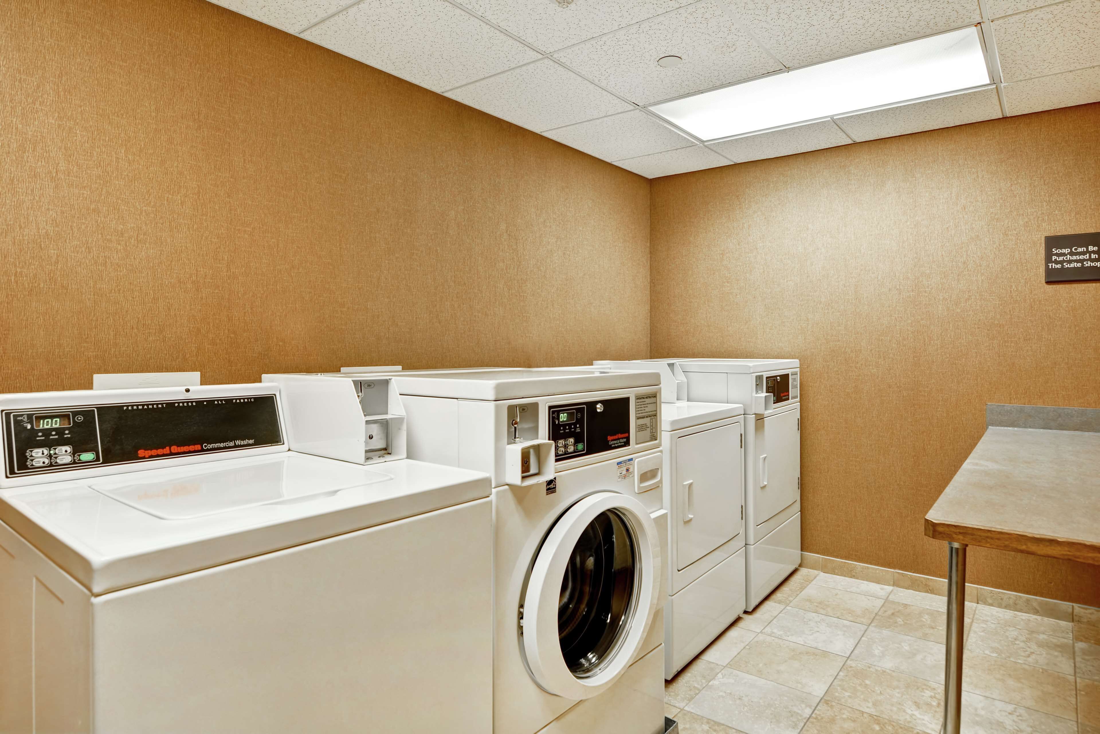 A hotel laundry room with multiple washing machines and dryers, a table, and a sign on the wall.