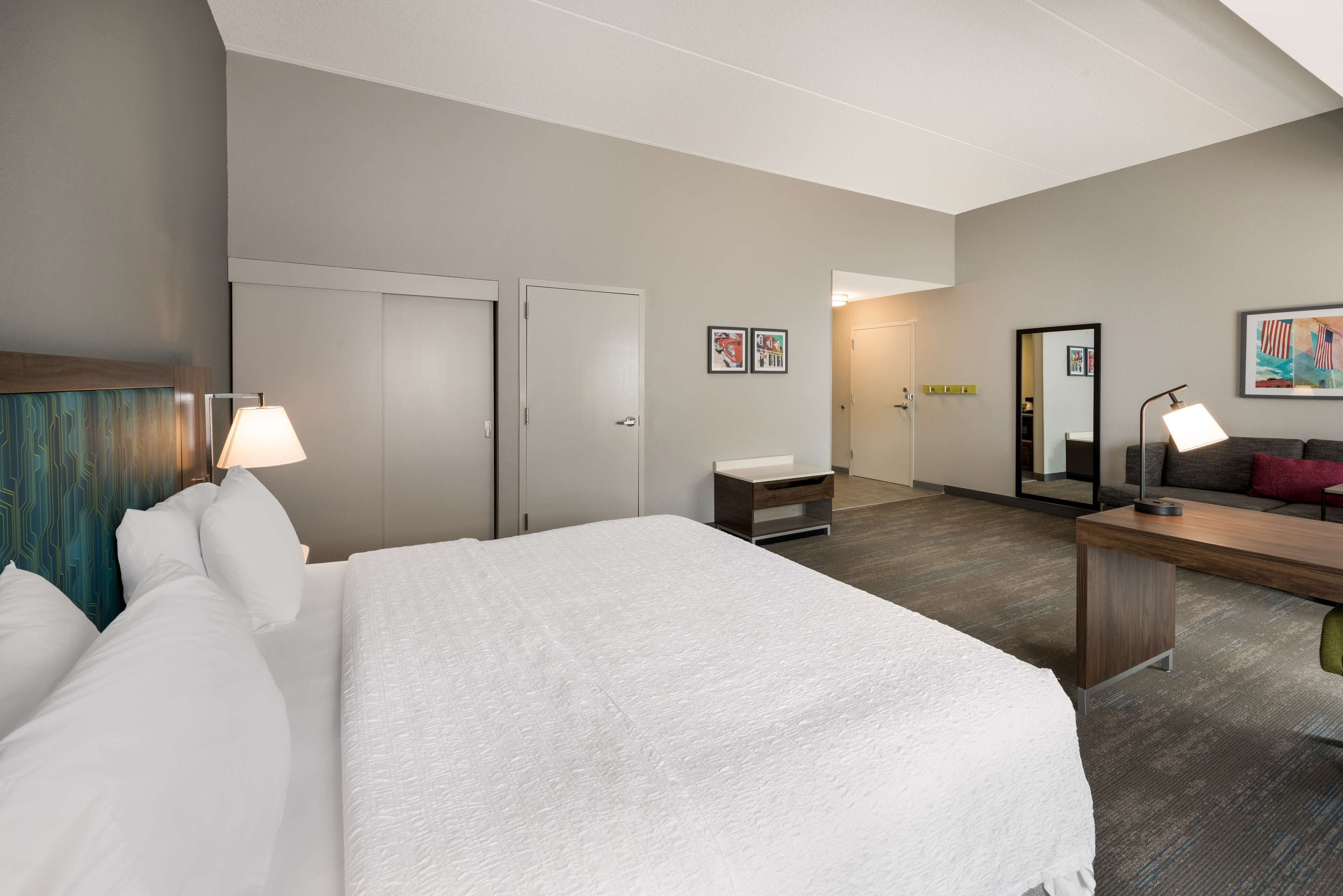 Une chambre d’hôtel avec un grand lit, des tables de chevet, un bureau, une chaise, un miroir et une porte.