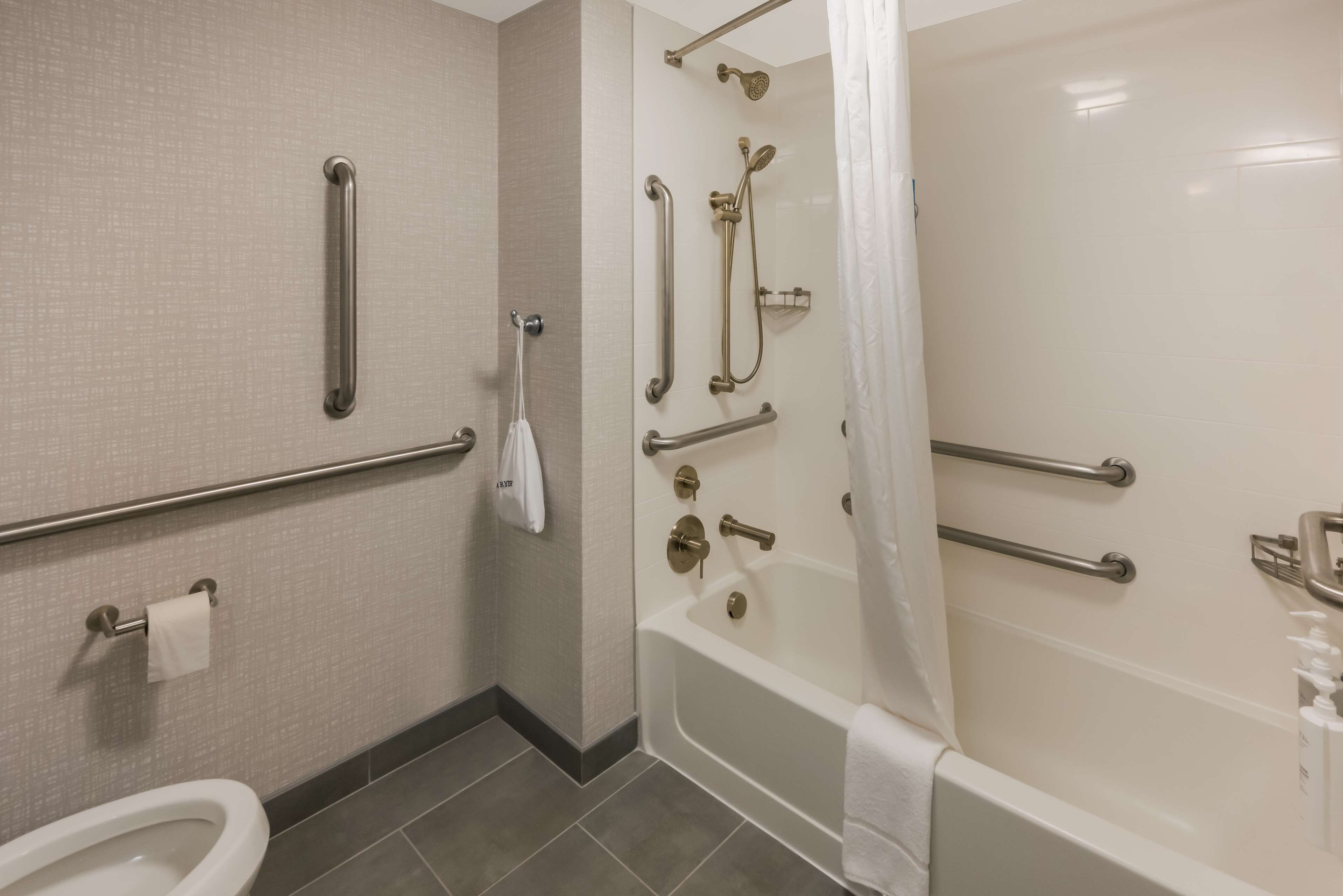 Une salle de bain équipée de toilettes, de barres d’appui, d’une douche avec un pommeau de douche amovible et d’une baignoire.
