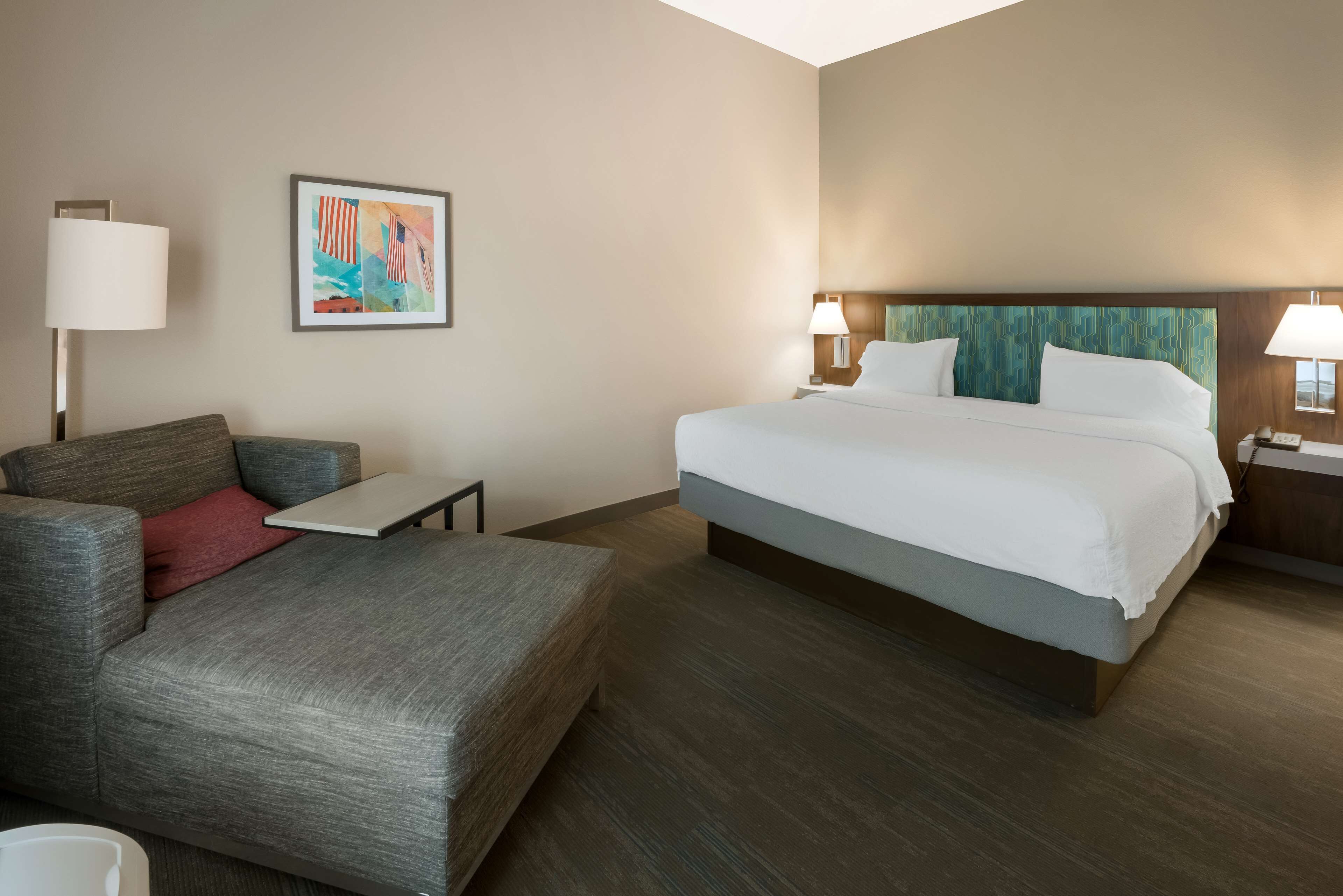 A hotel room with a large bed, a sofa, a small table, and a painting on the wall.