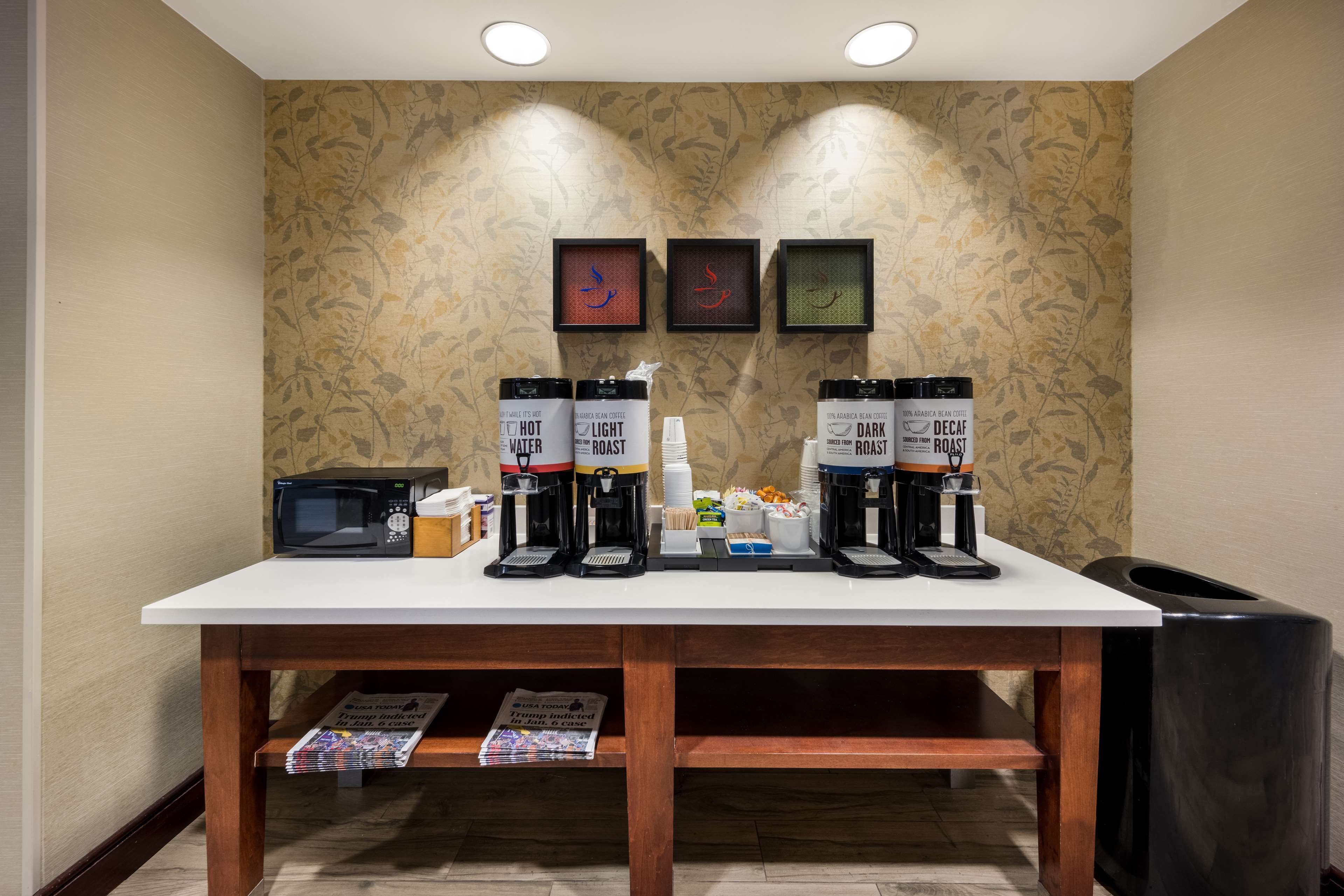Una estación de café con dos máquinas de café, un microondas y un cubo de basura.