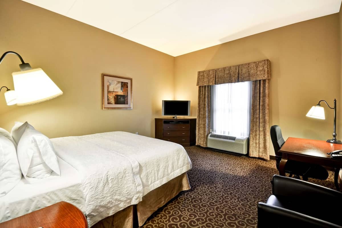 A hotel room with a bed, desk, chair, television, and a window with curtains.