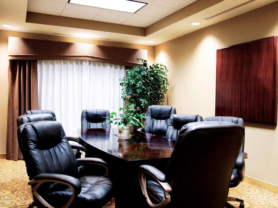 A conference room with a large table, six leather chairs, a potted plant, and a large wooden panel on the wall.