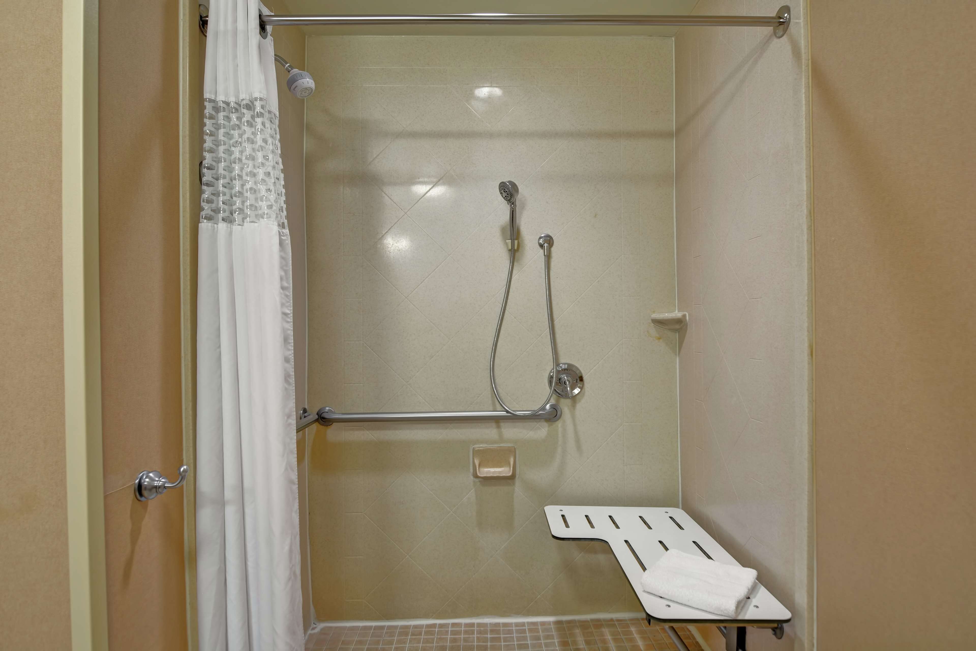 A shower area with a glass door, a grab bar, a handheld showerhead, and a towel rack.