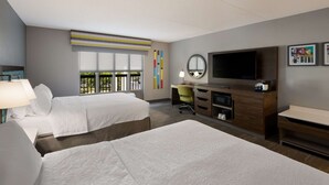 A hotel room with two beds, a desk, a TV, and a window with a view.