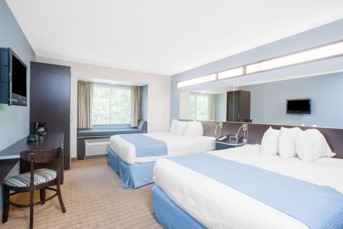 A hotel room with two beds, a desk with a chair, a TV, and a window with curtains.