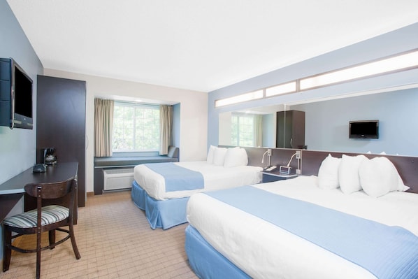 Habitación de hotel con dos camas, un escritorio con silla, televisión y ventana con cortinas.