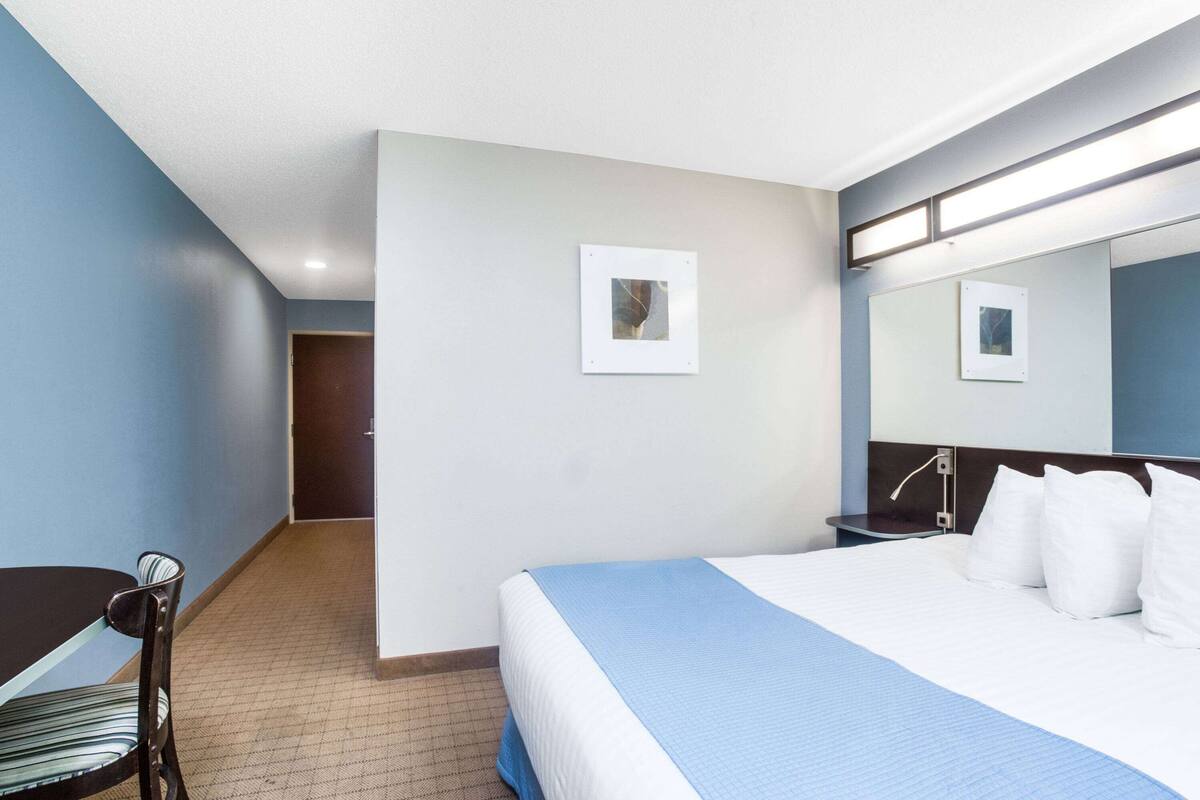 A hotel room with a bed, a desk, and a chair. There is a door leading to another room.