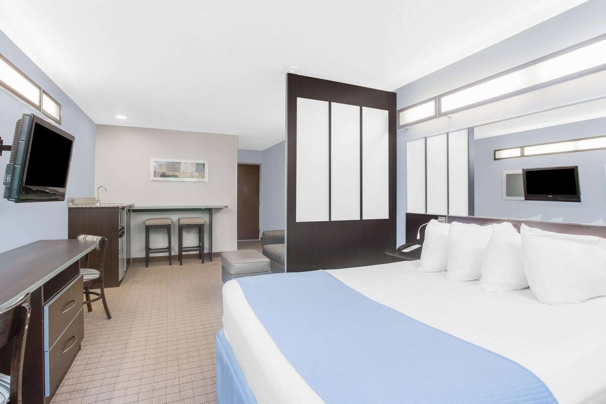 A hotel room with a bed, a desk, a TV, and a small kitchenette.