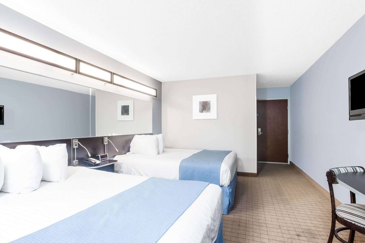 A hotel room with two beds, a desk, a chair, a TV, and a door.
