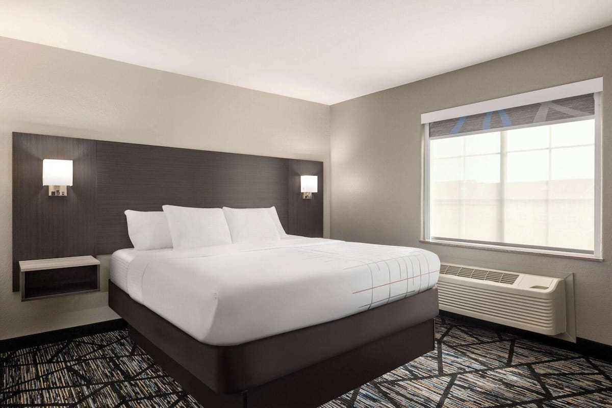 Une chambre d’hôtel avec un grand lit, deux tables de chevet, une fenêtre avec des stores, un radiateur fixé au mur et une moquette à motifs.