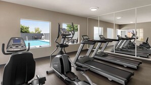 Academia com esteiras, elíptico e vista para a piscina.