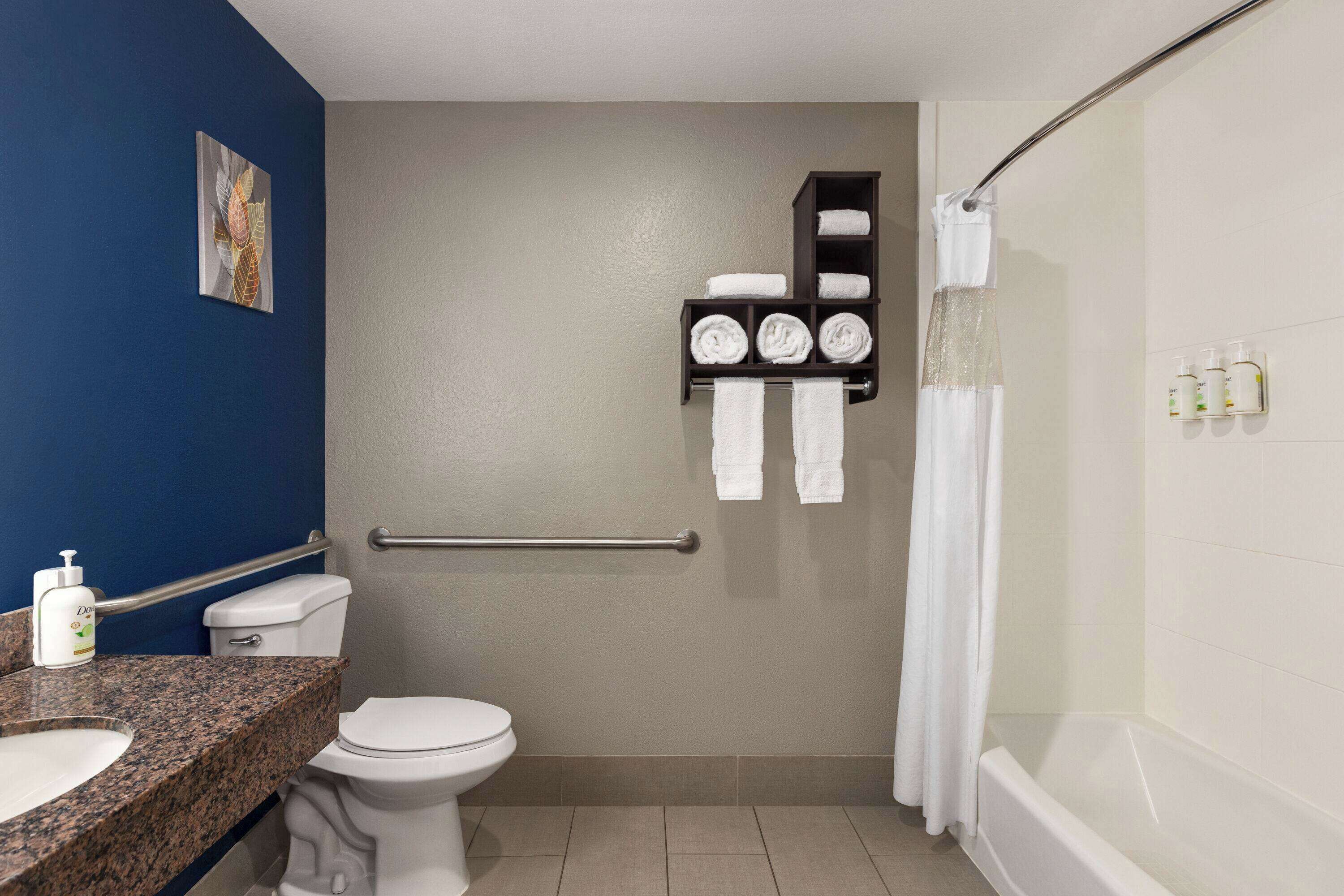 A bathroom with a toilet, sink, and bathtub. There is a handrail, a towel rack with towels, and a shower curtain.