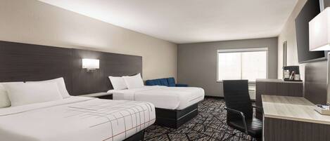 A hotel room with two beds, a desk, a chair, and a large window.