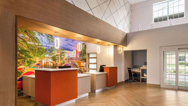 Uma área de recepção de hotel com um grande mural, balcões de madeira e um interior espaçoso.