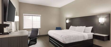 A hotel room with a bed, desk, chair, and a TV mounted on the wall.
