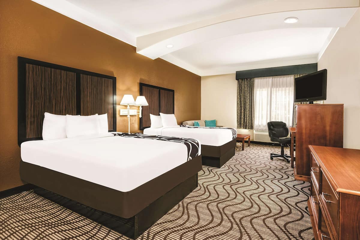 Une chambre d’hôtel avec deux lits, un bureau, une chaise, une télévision et une moquette à motifs.