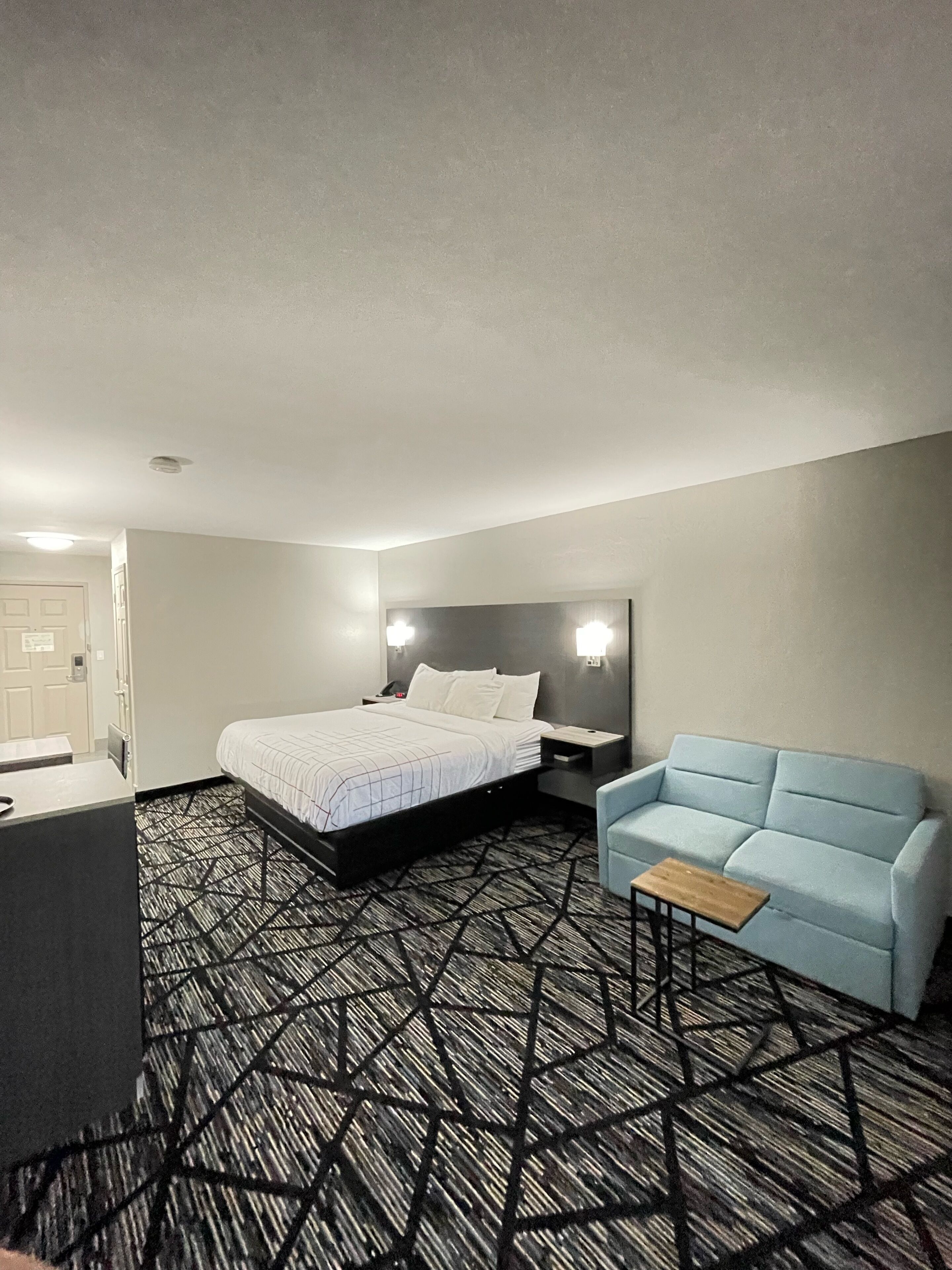 Habitación de hotel con una cama, mesitas de noche, un sofá y una alfombra estampada.