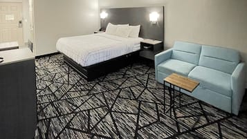 Habitación de hotel con una cama, mesitas de noche, un sofá y una alfombra estampada.