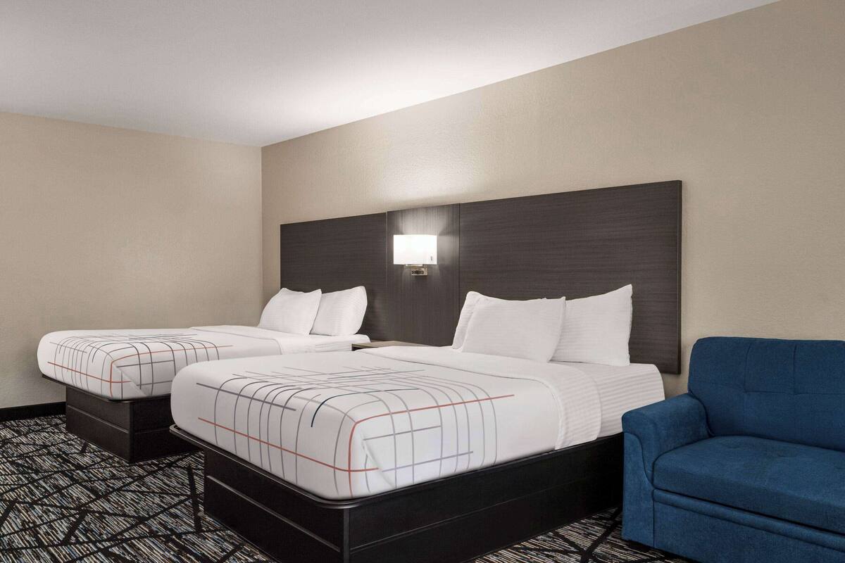 Une chambre d’hôtel avec deux lits, un fauteuil bleu et un luminaire fixé au mur.