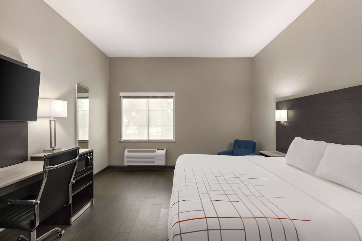 Une chambre d’hôtel avec un lit, un bureau, une chaise et une grande fenêtre.