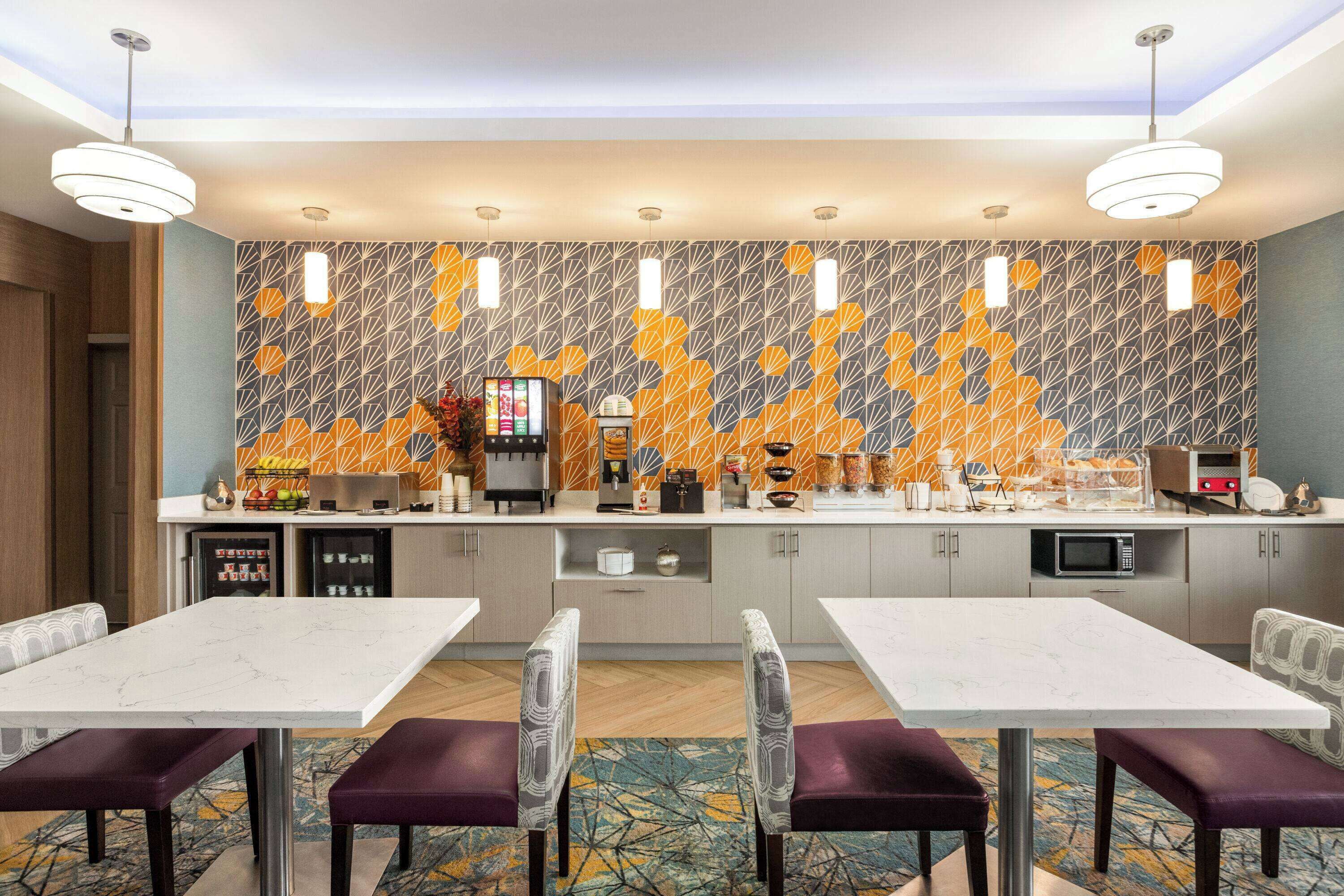 Una habitación de hotel moderna con zona de comedor, cocina con un salpicadero estampado y minibar.