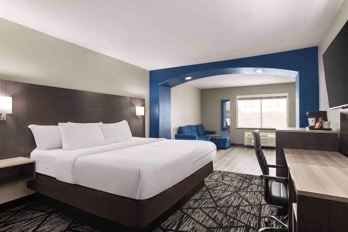 Une chambre d’hôtel avec un grand lit, un bureau, une chaise, un canapé bleu et une fenêtre donnant sur un beau paysage.