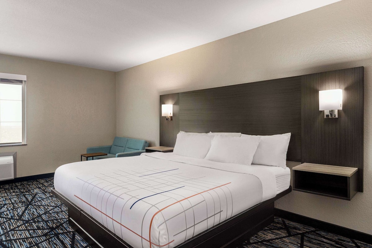 Une chambre d’hôtel avec un grand lit, deux tables de chevet, une chaise et un luminaire fixé au mur.