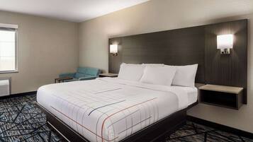 A hotel room with a large bed, two bedside tables, a chair, and a wall-mounted light fixture.