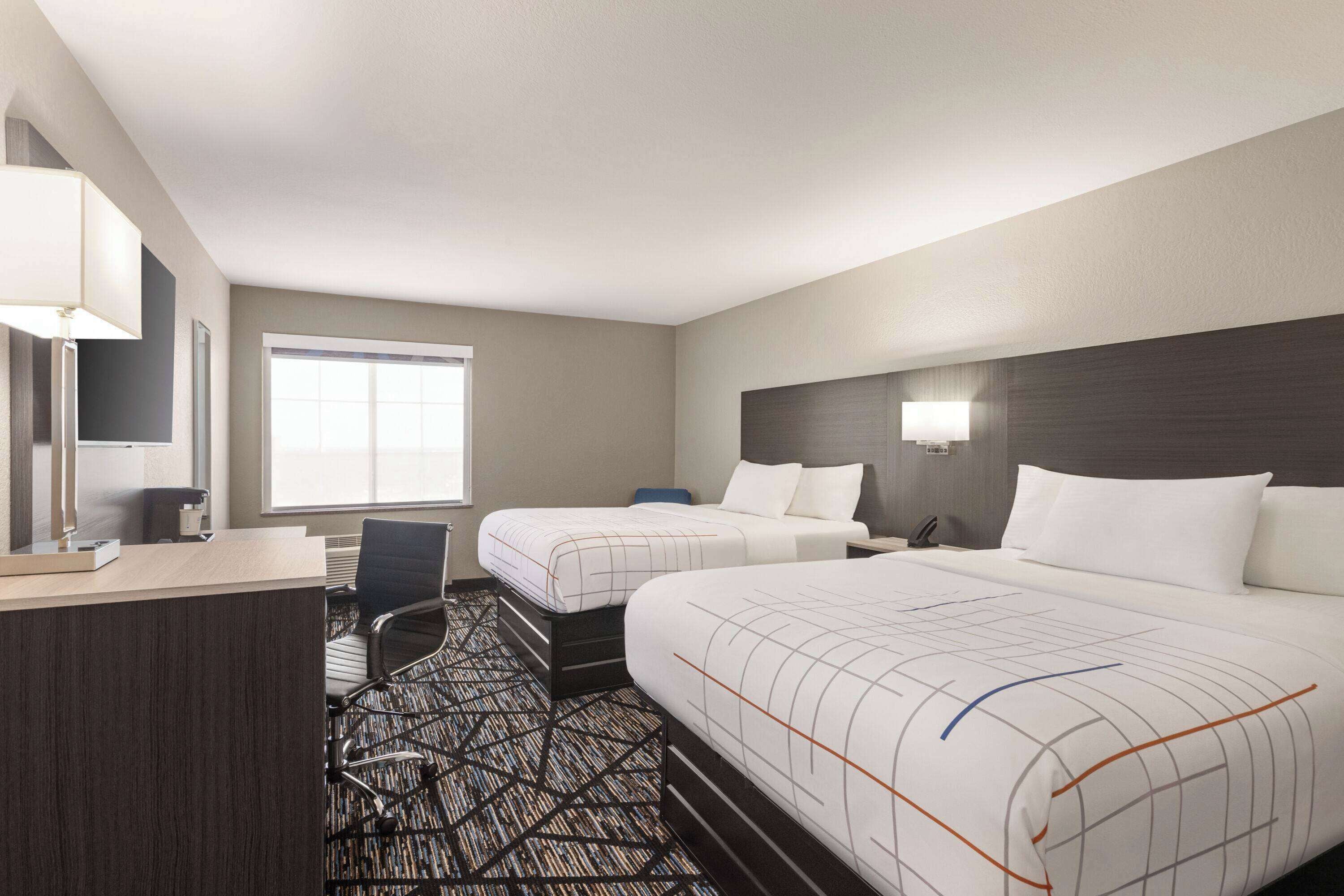 A hotel room with two beds, a desk, a chair, and a large window.