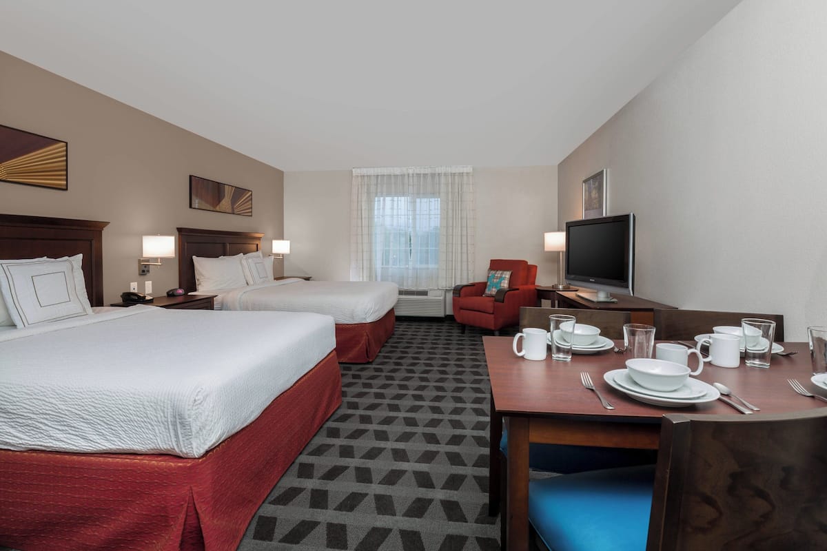 A hotel room with two beds, a desk with dining set, a TV, and a window with curtains.