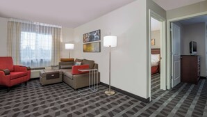 Ein Hotelzimmer mit einer Couch, einem Sessel und einem kleinen Tisch. Eine Lampe, ein Fernseher und ein Kleiderschrank sind vorhanden.
