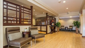 Eine großzügige Lobby mit einem hölzernen Empfangstresen, zwei Ledersesseln und einer Sitzecke mit einer Couch und einem kleinen Tisch.