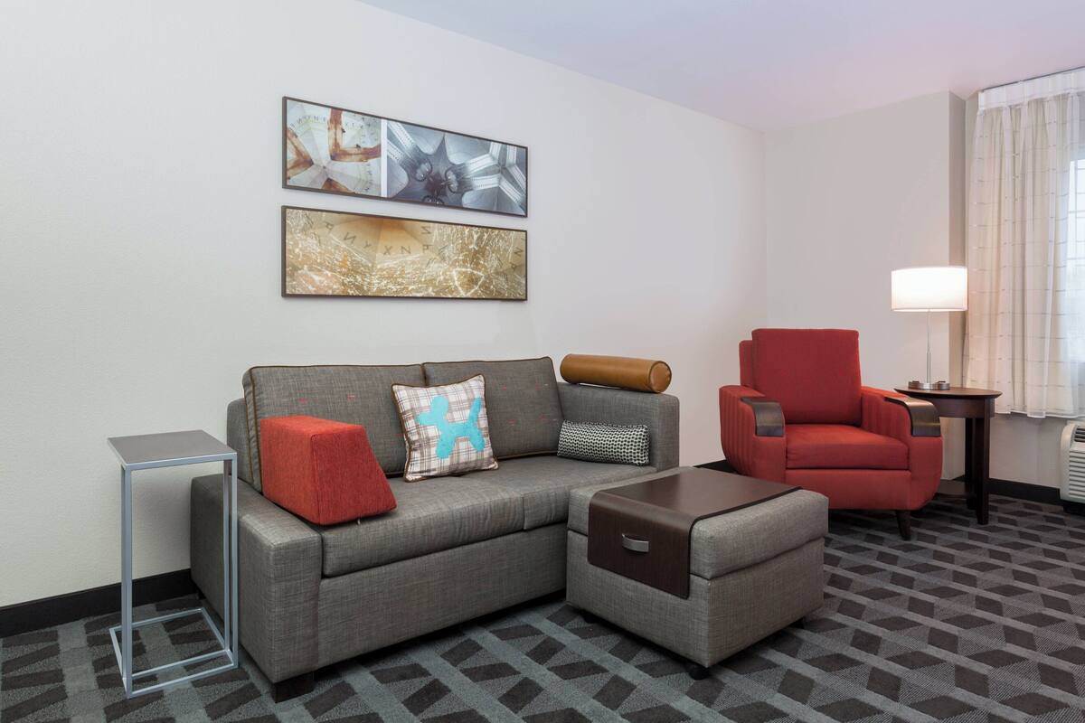 A modern hotel room with a grey sofa, a red armchair, a small side table, and a floor lamp.