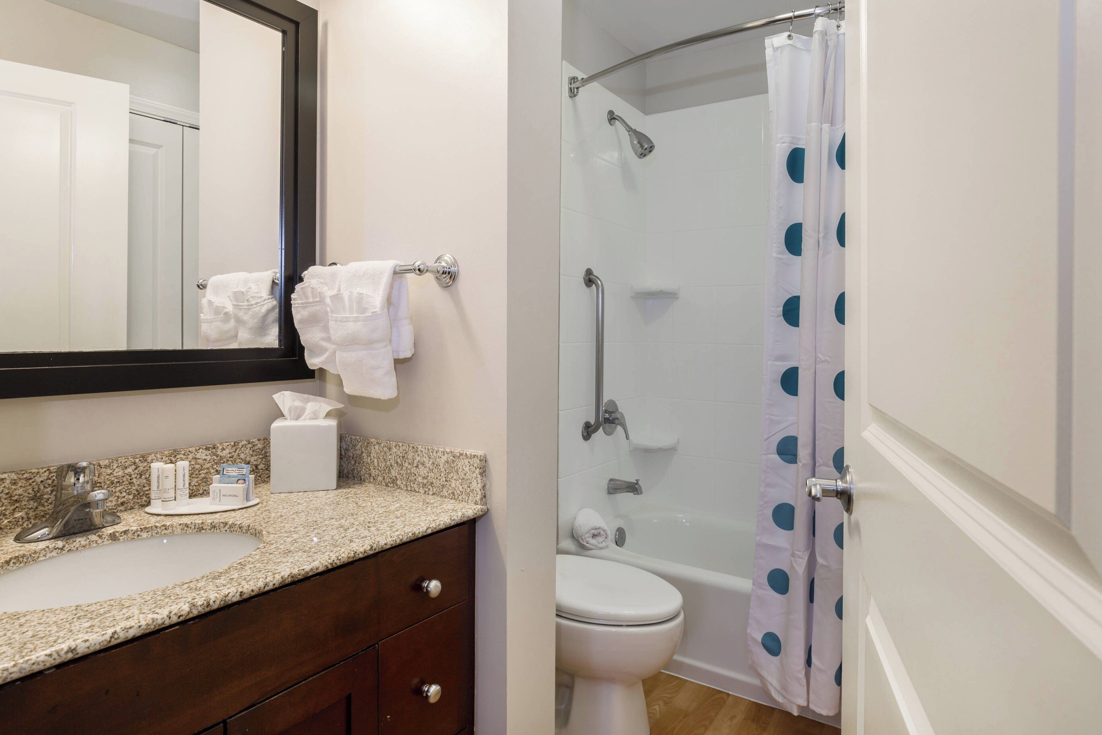 A bathroom with a sink, mirror, towel rack, toilet, and shower with a polka dot curtain.