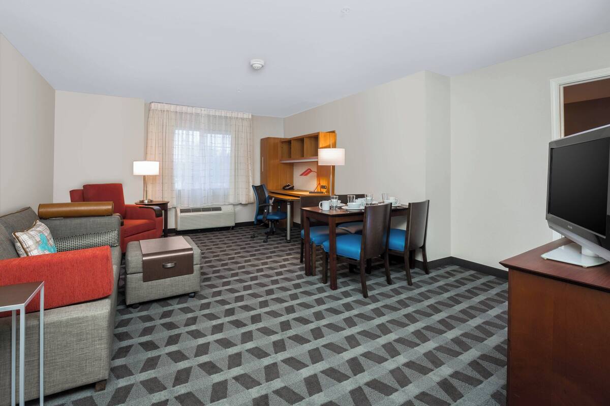 A hotel room with a sofa, armchair, desk, and television.